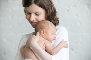 Young happy mother tenderly hugging her newborn baby