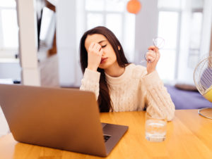 tired woman is working on her laptop and sitting at home at the wooden table