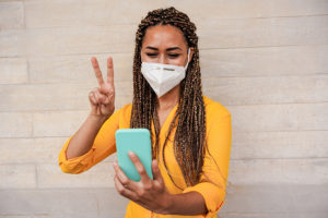 Young woman with braids doing video call while wearing face prot