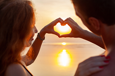 young sexu romantic couple in love happy on summer beach together having fun wearing swim suits showing heart sign on sundet