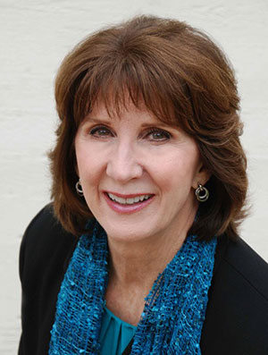 Dr. Laura Hauser, Ph.D. wearing blue blouse, blue scarf and black sweater, smiling.