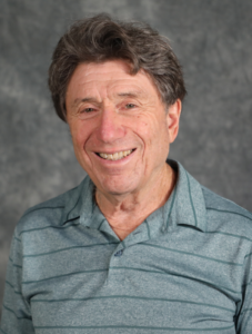 Man in a turquoise-gray shirt in front of a gray background.