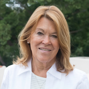 Woman wearing white in front of sand and a green tree background.